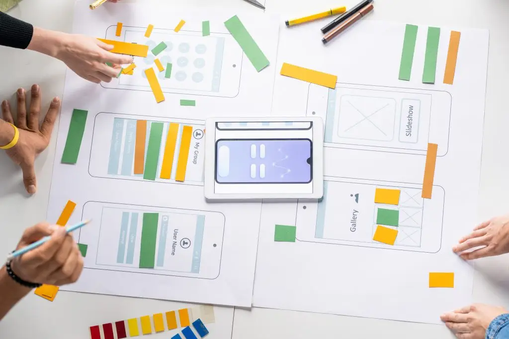 Mobile app design prototyping and planning process with sketches, sticky notes, and a smartphone mockup