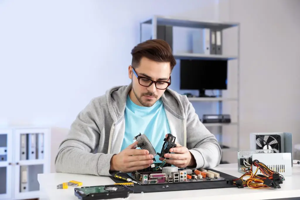 Man wearing glasses assembling computer parts at a table, demonstrating ITGuru Canada Inc.'s computer repair