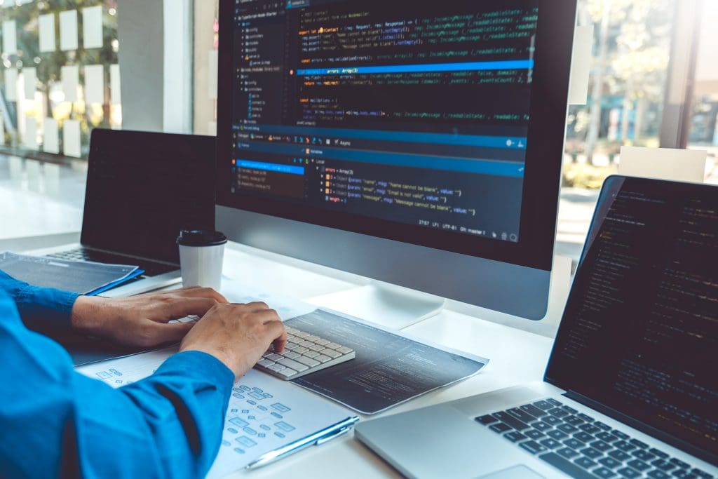 Software developer coding at desk with multiple monitors, illustrating website development and ongoing management services